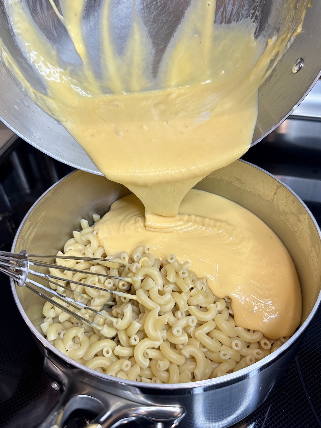 Pouring cheese sauce over cooked noodles