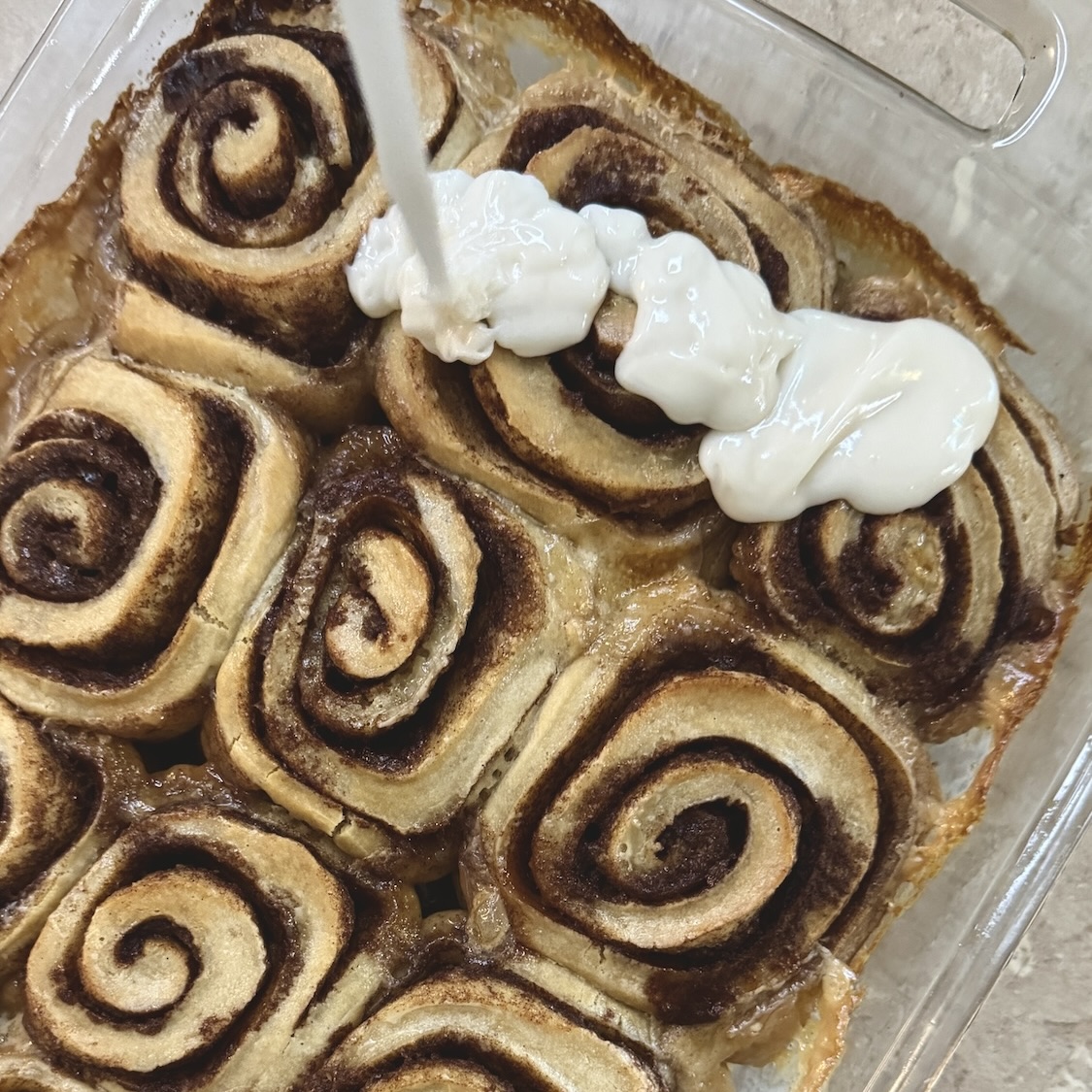 Drizzling icing over top of baked cinnamon rolls